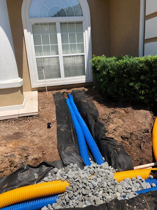 A trench with a French drain system being filled with rocks